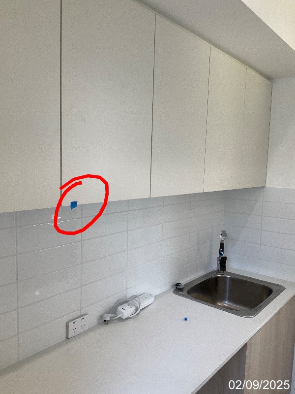 52_1_1756789297 - GoInspect Overhead laundry cupboard with the reported chipped lower door edge marked by a red circle and blue tape
