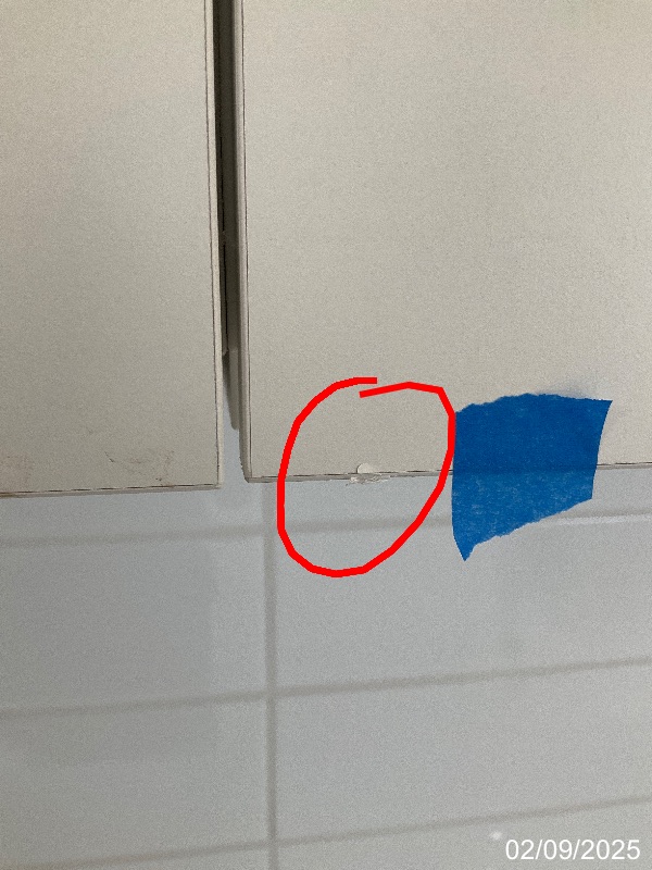 52_2_1756789299 - GoInspect Close-up of a chipped lower cabinet-door edge, marked with an original red circle beside blue tape