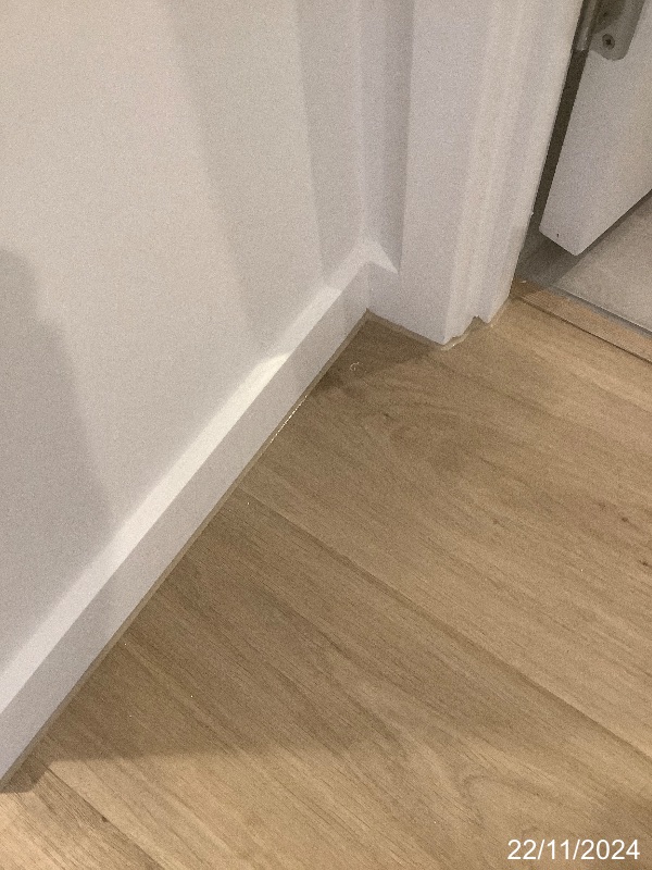 Hybrid flooring beside white skirting and a doorway during a handover inspection.