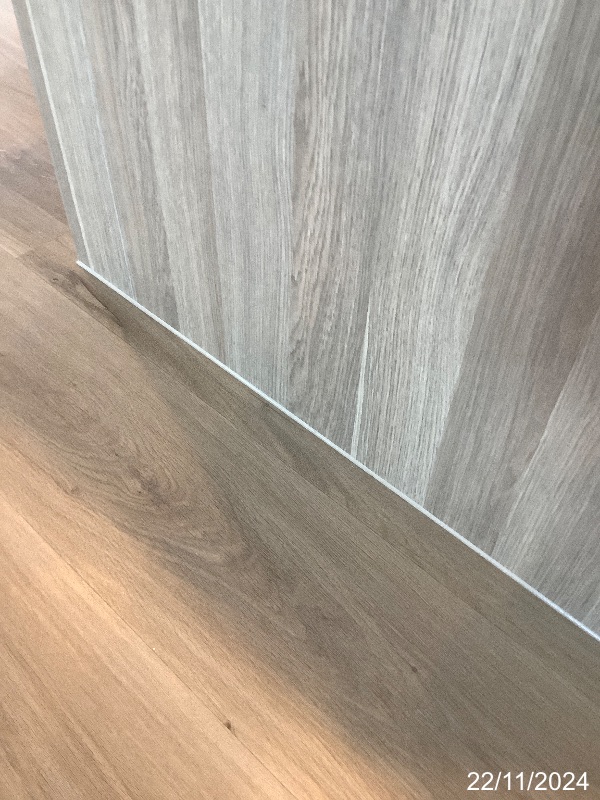 Hybrid flooring meeting a wood-look vertical panel, with white sealant along the junction.