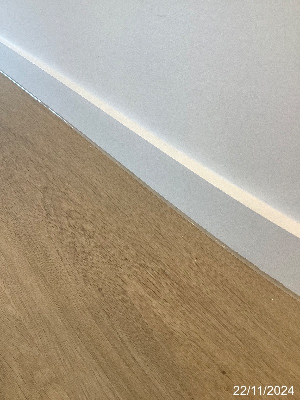 Hybrid flooring meeting white skirting, with visible sealant along the perimeter junction.