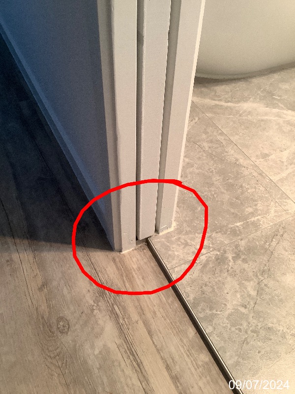 Red inspection circle around the base of a bathroom cavity sliding door at a tiled threshold