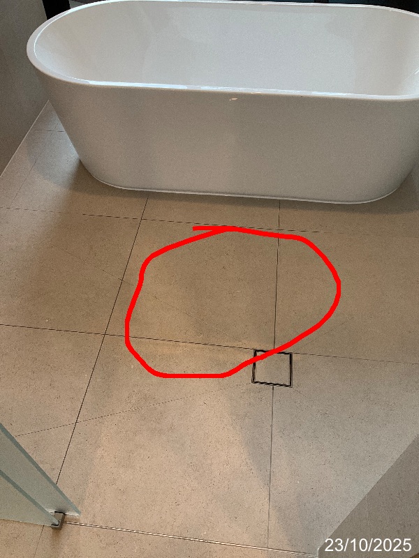 Marked area of water pooling on tiled shower-area floor beside a bath